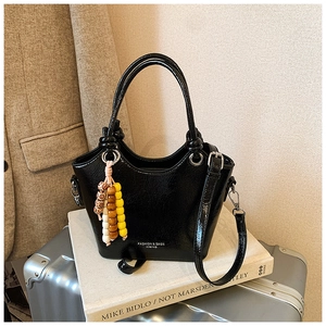Détail du sac seau noir brillant avec imprimé mode et pendentif à pompon en perles