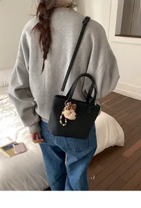 Close-up of black litchi grain bucket bag featuring a cute teddy bear plush charm