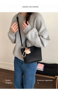 Detail of a black leather bucket bag with a cute plush bear charm and crossbody strap