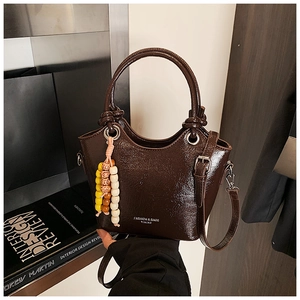 Détail du sac seau marron foncé brillant avec breloque perlée et bandoulière réglable