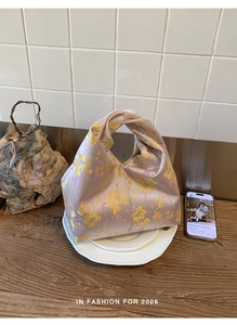 Nahaufnahme einer lavendelfarbenen Satin-Knotentasche mit goldenem Blumenmuster