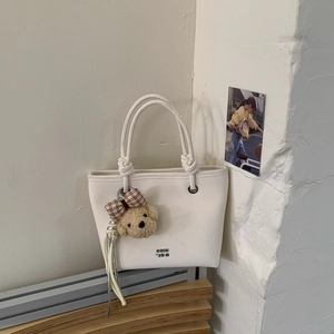 Detail of a beige bucket bag with knot handle and a cute brown plush bear charm