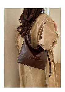 Detail view of a vintage dark brown leather tote bag on a woman wearing a camel trench coat