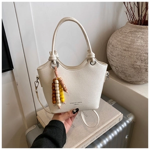 Détail du sac seau crème montrant la texture cuir litchi et le pompon en perles colorées