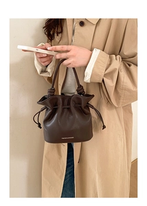 Detail of dark brown drawstring bucket bag featuring knot handle and brand lettering