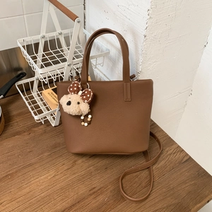 Close-up of brown textured leather tote bag featuring a cute plush animal pendant detail