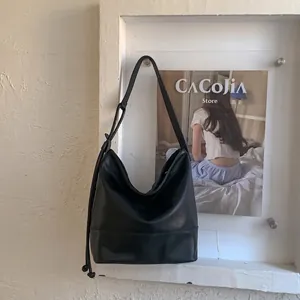 Detail of a large black matte leather bucket bag with side drawstring and adjustable strap