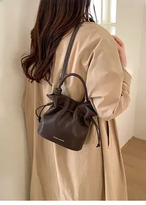 Detail of a dark brown drawstring bucket bag with elegant leather texture and shoulder strap