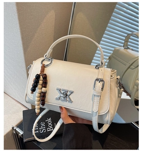 Détail d'un sac à main en similicuir crème avec logo argenté et gland en perles de bois