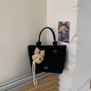Detail of black suede bucket bag featuring a plaid bow bear charm and elegant fringe