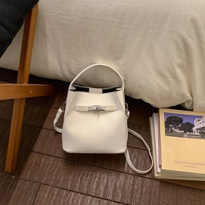 Detailed close-up of a cream white bucket bag with metallic buckle on a wooden floor