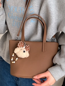 Brown litchi grain leather tote bag with a cute teddy bear charm for daily commuting
