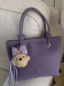 Chic purple lychee texture bucket bag with knot handle and cute dog charm on white sofa