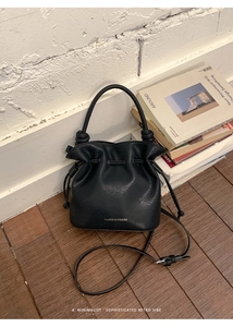 Detail of black drawstring bucket bag with silver brand logo and knotted handles