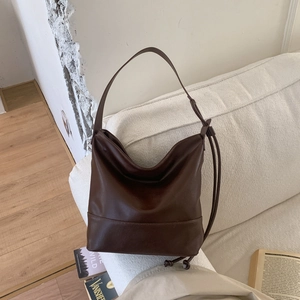 Detail view of smooth dark brown leather bucket bag on a white sofa with retro style
