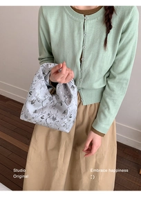Detail der hellblauen Stoff-Eimertasche mit Blumenmuster und Mintgrüner Strickjacke