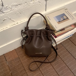 Detail of dark brown drawstring bucket bag with textured leather and brand lettering