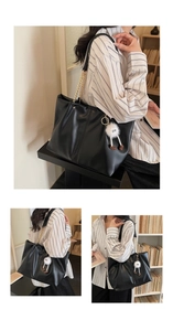 Detail of black pleated tote bag featuring gold chain strap and plush monster charm