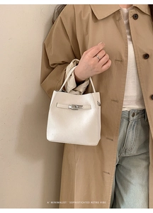 Detail of pearl white bucket bag with silver turn-lock clasp on a beige trench coat