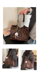 Detail view of large brown tote bag with gold chain handles and cute plush monster charm