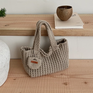 Détail du sac cabas beige tricoté main avec texture ondulée et étiquette en cuir