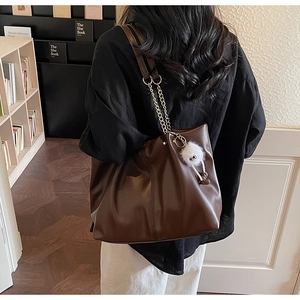 Detail of dark brown vintage soft leather tote bag with metal chain strap and furry charm