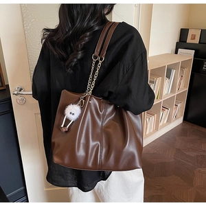 Detailed close-up of dark brown faux leather tote with chain straps and plush charm