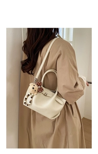 Detail of cream white pebbled leather bucket bag featuring a cute plush bear pendant