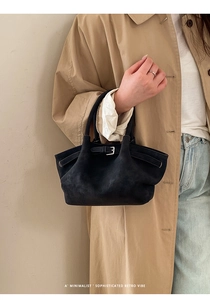 Detailed view of black suede bucket bag with decorative buckle and slim handle strap