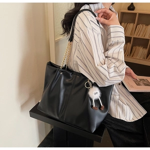 Detail of soft black leather tote bag featuring golden metal chain and plush eye pendant
