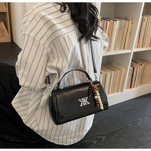 Détail d'un sac baguette noir brillant avec boucle argentée en X et breloque en perles
