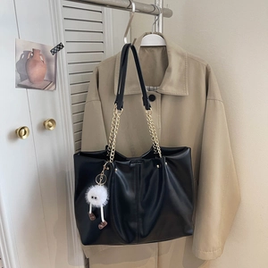 Detail of black faux leather tote bag featuring gold chain straps and white plush charm