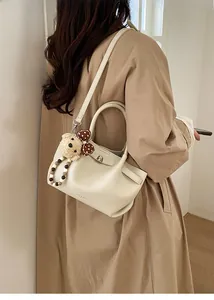 Detailed side view of off-white lychee grain leather bucket bag with plush bear charm