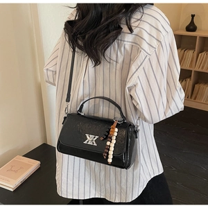 Vue détaillée du sac baguette noir brillant avec boucles argentées et breloque perlée