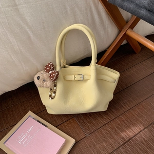 Detail view of yellow pleated bucket bag with cute brown plush bear charm and bow