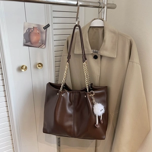Detail of vintage brown tote bag with gold chain strap and cute white monster charm