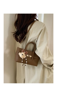 Close-up of brown litchi grain leather baguette bag with a cute plush bear pendant