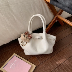 Detail of white pleated bucket bag with metal buckle and plush bear charm on wood floor