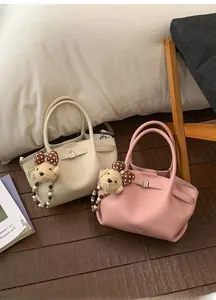 Detail view of bucket bag with lychee texture, metal lock, and plush teddy bear charm