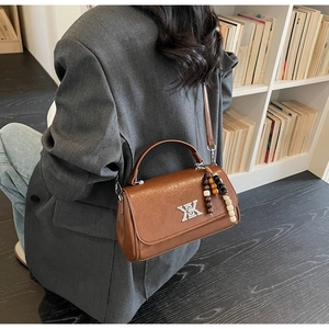 Détail d'un sac en cuir marron avec boucle en métal argenté et breloque en perles colorées