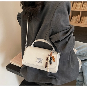 Détail du sac baguette blanc cassé avec lettres argentées et breloque en bois