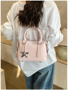 Detail of light pink Boston bag with star charm worn by a model in casual white shirt