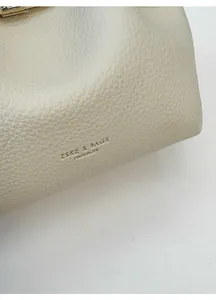 Close-up of off-white lychee grain leather texture with gold stamped brand logo on the bag