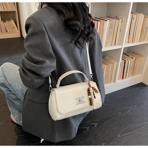 Détail d'un sac baguette blanc avec boucle en métal argenté et breloque en perles