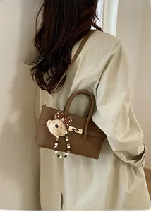 Close-up of brown textured leather handbag featuring a cute teddy bear charm and gold clasp