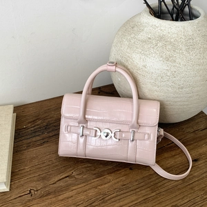 Dettaglio borsa rosa con trama coccodrillo e fibbia a cuore su tavolo in legno rustico