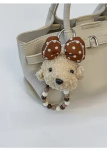 Close-up of fluffy teddy dog plush charm with polka dot bow on a beige leather tote bag