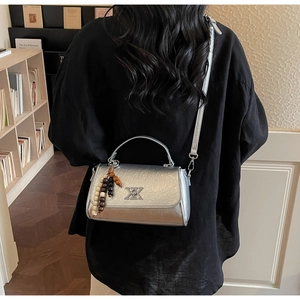 Sac bandoulière argenté avec boucle X et breloque perlée porté sur chemise noire