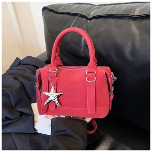 Close-up of red leather Boston bag with silver star pendant and dual handle detail