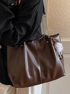 Deep brown leather tote bag with gold chain straps and a fluffy pom-pom pendant